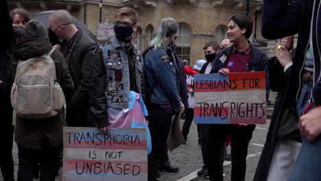 Eine-Zeitlupenaufnahme-Von-Zwei-Personen,-Die-Bei-Einer-Protestkundgebung-Stehen-Und-Plakate-In-Den-Farben-Der-Trans-Rechte-Halten,-Auf-Denen-Steht:-„Transphobie-Ist-Nicht-Unvoreingenommen“-Und-„Lesben-Für-Trans-Rechte“.