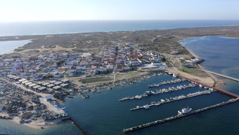 Barcos-Amarrados-En-El-Muelle-De-La-Isla-De-Culatra-Con-Pueblo-Costero-Durante-El-Día-En-Algarve,-Faro,-Portugal