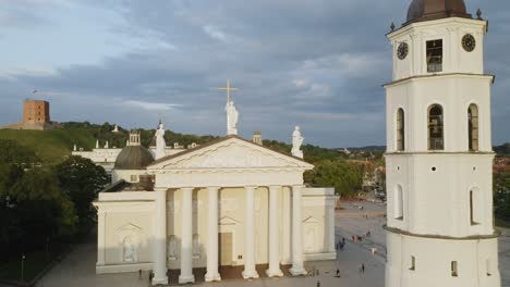 AERIAL:-Pedestal-Shot-of-Vilnius-Cathedral-and-Bell-Tower-with-Blue-Sky-in-Background-and-People-Walking-on-Ground
