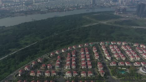 Aerial-view-of-ultra-modern-lakeside-housing-and-apartment-development-on-a-sunny-day-starting-with-city-and-river-and-park,-green-space,-road-and-new-villas-tilting-to-top-down-of-development