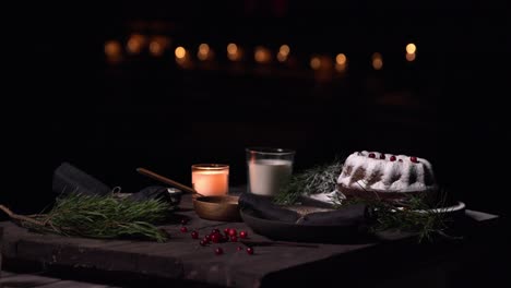 Isolated-dark-food-christmas-table-set-with-candles,-dessert-cake-with-cream-of-tartar-powder,-pine-leaves-and-red-berries-fruits