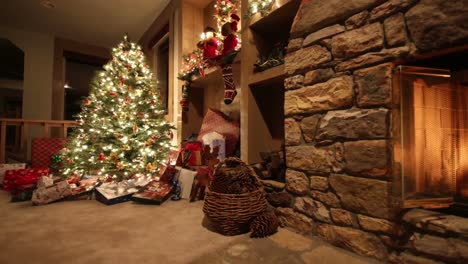 Christmas-tree-decorated-with-light-near-a-stone-fireplace,-a-basket-full-of-pine-cone,-presents-and-figurines-warm-scene