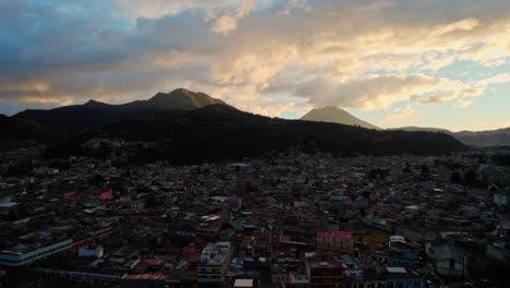 Drohnen-Luftaufnahme-Des-Städtischen-Kolonialen-Stadtbildes-In-Der-Nähe-Von-Zwei-Vulkanen-Während-Der-Goldenen-Stunde-Bei-Sonnenuntergang-In-Quetzaltenango-Xela,-Guatemala
