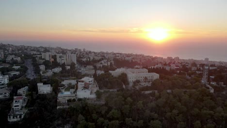 City-with-buildings-and-garden-on-the-edge-of-the-coast-at-colorful-sunset,-sea-in-the-background,-Israel