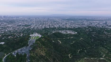 Aerial-Shot-of-Griffith-Observatory-Overlooking-Los-Angeles-and-Hollywood-on-Overcast-Day,-Hiking-Trails-Below