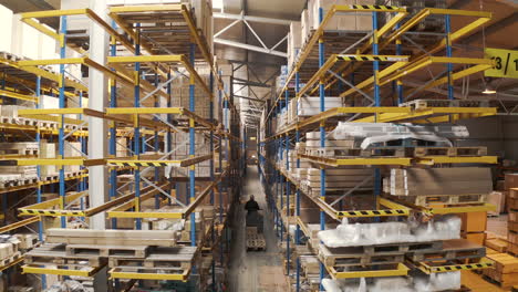 Man-driving-an-electric-storage-cart-through-a-warehouse-aisle,aerial