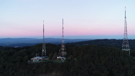 Smooth-aerial-reveal-of-TV-towers-standing-tall-on-mountain-hill-side