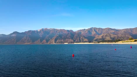 Luftaufnahme-Von-Atemberaubendem-Blauem-Wasser-Im-Lake-Hawea-In-Neuseeland-Und-Wilden-Steilen-Hügeln-Im-Hintergrund