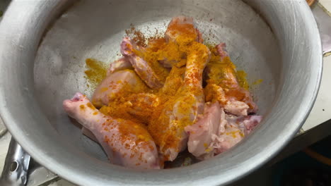 Slow-Dolly-Out-From-Raw-Chicken-Leg-Pieces-Sprinkled-With-Spice-In-Metal-Bowl-In-Kitchen