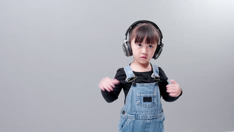 Child-listening-to-music-with-headset-wearing-jeans-on-gray-background-in-studio