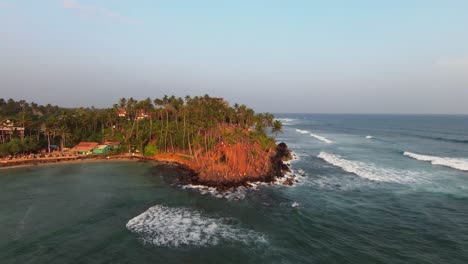 Aerial-shot-of-people-standing-near-the-rocks-and-the-palm-tree-island