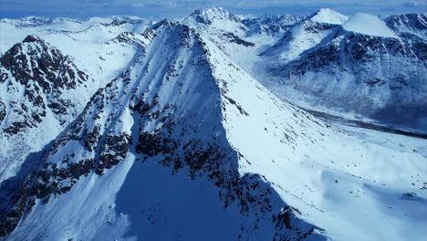 Panorama-Aéreo-Ascendente-Disparado-Sobre-El-Paisaje-Nevado-De-Montaña-Durante-El-Sol-Y-El-Cielo-Azul-En-Invierno---Isla-Vesterålen-En-Noruega