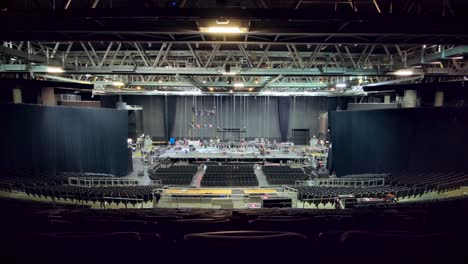 Camera-tilts-down-to-workers-setting-up-equipment-on-a-large-concert-stage