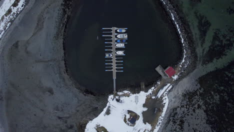 Aerial-dolly-shot-of-Ase-harbor-looking-down-onto-boats-the-dock-and-breakwater-with-light-snow-and-black-water
