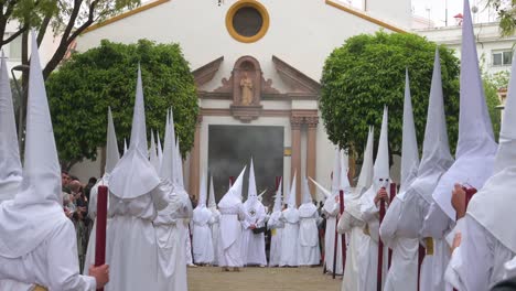 Penitents-gather-outside-their-brotherhood-church-during-a-procession-as-they-celebrate-the-Holy-Week-in-Seville,-Spain
