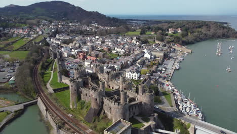 An-aerial-view-of-Conwy-Castle-on-a-sunny-day,-flying-away-from-the-castle-with-the-town-in-the-background,-North-Wales,-UK
