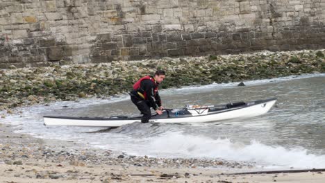Male-in-safety-life-jacket-preparing-kayak-on-Welsh-seaside-waves