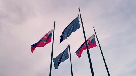 Die-Flaggen-Der-Slowakei-Und-Der-Europäischen-Union-Flattern-Nebeneinander-Im-Wind-Am-Fahnenmast,-Zeitlupenansicht-Aus-Niedrigem-Winkel