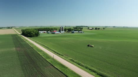 Aerial-panorama,-tractor-spraying-pesticide-onto-fresh-crops-in-farmland-countryside