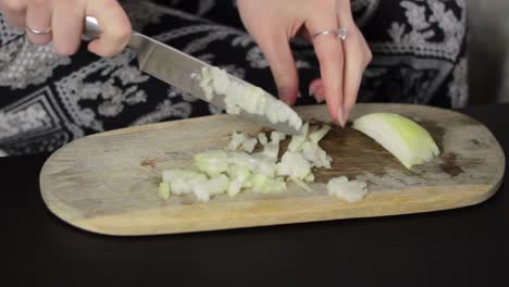 A-woman's-hands-chopping-a-onion-on-a-wooden-cutting-board-with-a-sharp-knife,-static-close-up