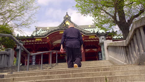 ASAKUSA,-TOKYO,-JAPAN-circa-April-2020:-man-climbing-up-the-stairs-to-pray-at-traditional-Japanese-temple,-fresh-green-tree-approach-in-peaceful-and-quiet-zen-style-garden-on-a-sunny-spring-day