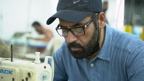 Portrait-Of-A-Man-Sewing-In-A-Industrial-Clothing-Manufacturing-Factory,-Pakistan