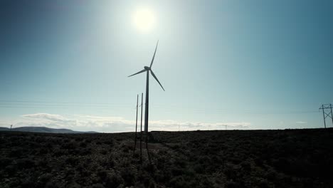 Backlit-silhouette-of-a-giant-electric-wind-generator,-carbon-neutral-energy,-aerial-orbit
