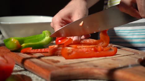 Person-Schneidet-Rote-Paprika-Mit-Messer-Auf-Schneidebrett-In-Der-Küche
