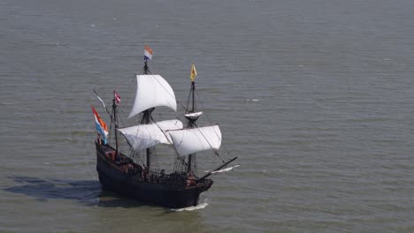 Replica-of-historic-VOC-ship-sailing-in-open-seas,-Dutch-flags-flutter