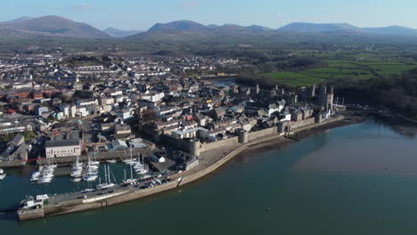 An-aerial-view-of-the-town-of-Caernarfon-on-a-sunny-day,-flying-left-to-right-over-the-seafront-and-harbour-area,-Gwynedd,-North-Wales,-UK