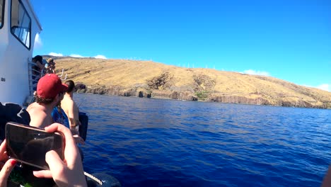 People-on-a-whale-watching-boat-holding-up-cell-phone-cameras-and-pointing-at-a-mom-and-baby-humpback-whale-during-peak-migration-season-in-Maui