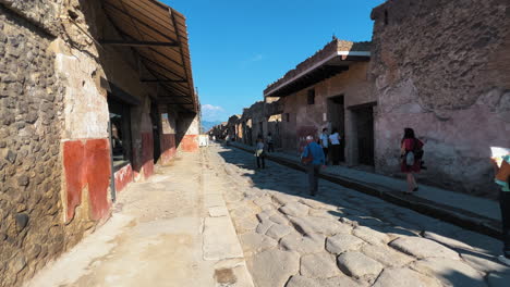 Dolly-forward-walk-between-old-street-in-Pompeii-with-ruins-and-historic-buildings-during-summer---Tourist-enjoying-sightseeing-trip-in-italy