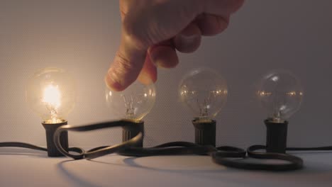 Four-filament-bulbs-being-switched-on-by-a-hand