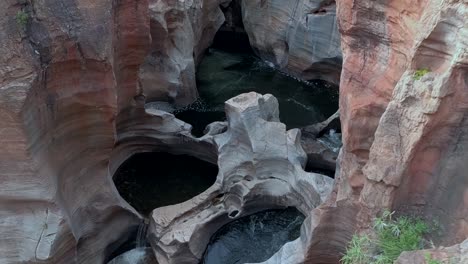 Desending-aerial-HD-drone-footage-of-beautiful-natural-rock-formations,-Bourke's-Luck-Potholes,-hewn-by-centuries-of-water-flow-by-the-Blyde-River-in-Graskop,-Mpumalanga,-South-Africa