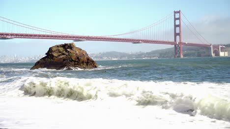 Blick-Auf-Die-Golden-Gate-Bridge-Und-Die-Wellen,-Die-Am-Ufer-Brechen,-Und-Einen-Großen-Felsen