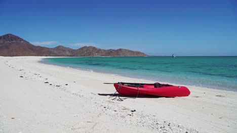 A-kayak-pulled-up-on-a-white-sand-beach-at-a-calm-water-bay-in-a-tropical-paradise