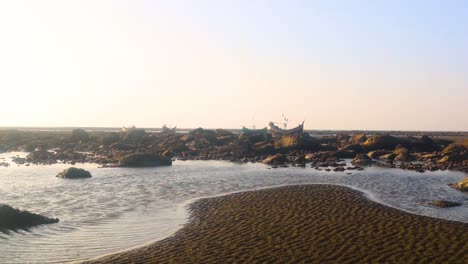 Tide-pools-at-low-tide-on-a-rocky-shoreline-with-fishing-boats-in-the-background