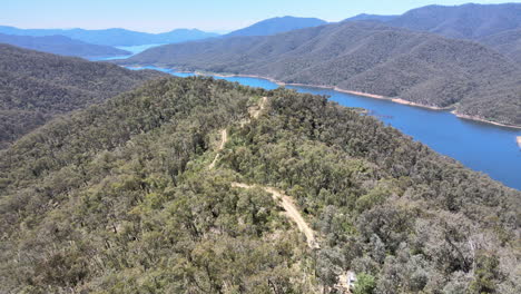 Slow-moving-high-drone-shot-emerging-from-trees-to-show-mountains-blue-water-near-Lake-Eildon,-Victoria-Australia