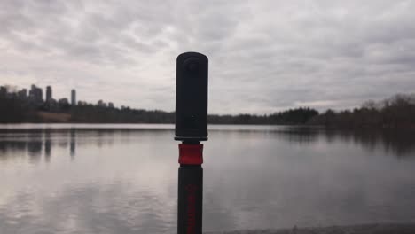 360-camera-on-monopod-on-the-edge-of-a-lake-capturing-landscape-photography-videography-of-water-clouds-trees-sky
