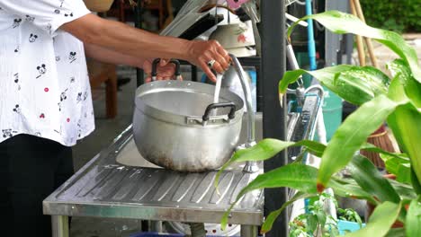 Person-washing-stainless-steel-pot-in-garden-kitchen,-handheld-view
