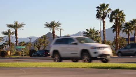 Car-traffic-on-palm-tree-lined-avenue,-La-Quinta,-California-suburbs-in-sunshine