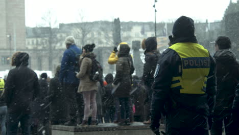 Wide-shot-of-a-police-office-on-duty-among-crowds-of-people-for-the-Covid-19-protests,-cold-snowy-day