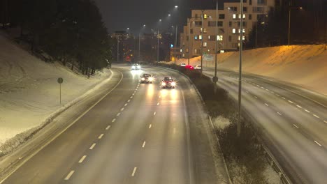 Wide-shot-of-a-quite-nighttime-highway-on-a-cold-snowy-night,-vehicles-driving-in-both-directions