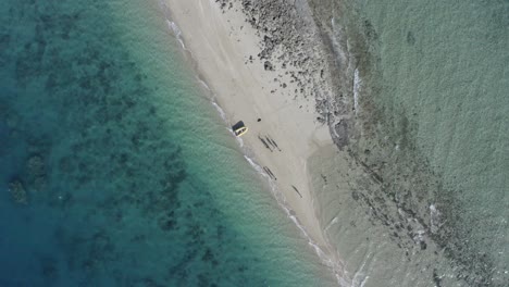 Absteigende-Luftaufnahme-Von-Menschen-Und-Schlauchboot-Auf-Einer-Kleinen-Koralleninsel