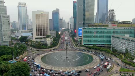 Rush-hours-in-Jakarta-downtown-by-Selamat-Datang-Monument,-aerial-view