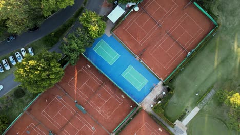 Aerial-top-down-rising-above-clay-tennis-courts-and-a-professional-golf-course-on-a-sport-club-at-sunset