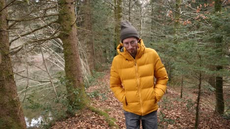 White-male-with-bright-yellow-coat-walks-in-moody-Swiss-forest,-tracking-infront