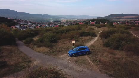 Aerial-view-of-a-blue-Ford-Puma-parked-next-to-a-country-crossroads,-on-top-of-a-hill