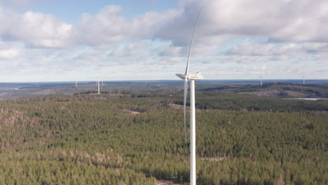AERIAL---Wind-turbines-in-a-forest-wind-power-farm,-Sweden,-wide-circle-shot