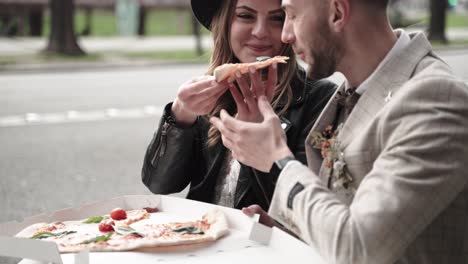 Retro-styled-wedding-couple-with-black-leather-jacket-sitting-in-the-streets-while-bride-feeding-her-groom-with-pizza